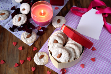 White cookies with almond in a heart-shaped box. Tiny hearts are scattered around. Treats for Valentine's Day