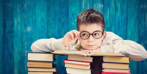 eight years old child reading a book at home. Boy studying at table on blue background