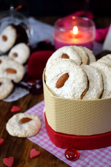 White cookies with almond in a heart-shaped box. Tiny hearts are scattered around. Treats for Valentine's Day