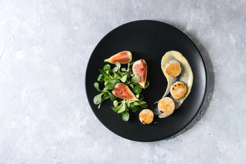 Fried scallops with lemon, figs, sauce and green salad served on black plate over gray texture background. Top view, copy space. Plating, fine dining - 188832423