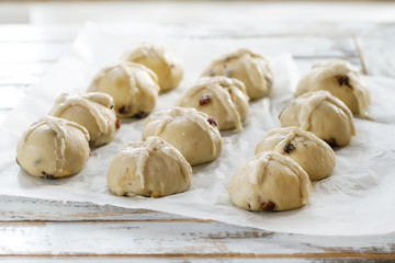 Raw unbaked buns. Ready to bake homemade Easter traditional hot cross buns on baking paper over white wooden table with window at background. Natural day light. Rustic style.
