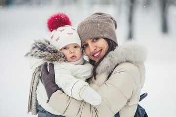 Fototapeta na wymiar Close up brunette young women portrait with baby girl, daughter hugs and smiling in snowy park.
