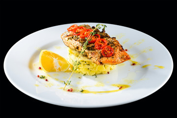 Traditional Italian cuisine. Grilled delicious salmon with lemon and chile in a white plate on dark background.