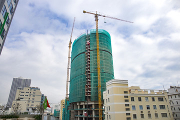 Fototapeta premium construction of a high-rise building in scaffolding and two yellow construction cranes on the background of the blue cloudy sky