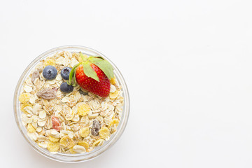 Healthy Breakfast Concept: a bowl of oat muesli with candied fruit and fresh strawberry and blueberries on white, top view, copy space
