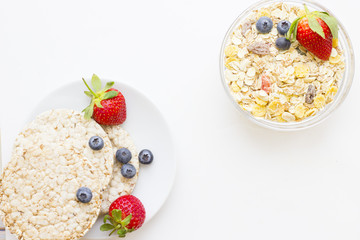 Healthy Breakfast Concept with a plate of wheat breadcrisps with fresh strawberries and blueberries and oat muesli with candied fruit on white, view from above
