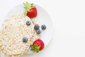 Healthy Breakfast Concept with a plate of wheat breadcrisps with fresh strawberries and blueberries on white, view from above, copy space