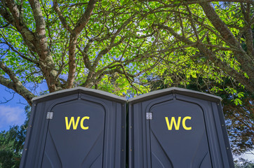 Zwei moderne Toilettenkabinen aus Kunststoff im Schatten unter Bäumen aufgestellt - Two modern...