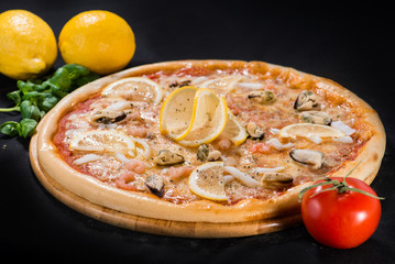 Delicious juicy Sea pizza with shrimps, lemon and pineapple on wooden board on dark background