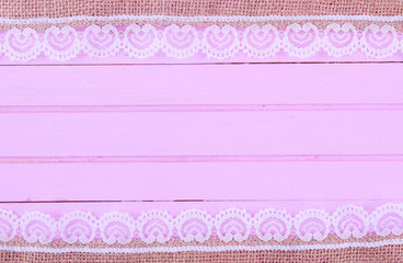 Burlap lace on pink wooden background