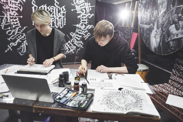 Portrait of the masters of calligraphy. Tattoo artists make a sketch sitting at the table in the...