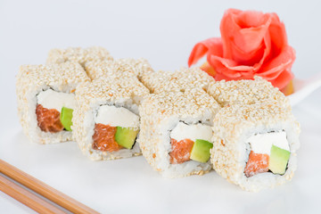 Delicious sushi rolls with rice, cream cheese, salmon, avocado and sesame seeds on light background
