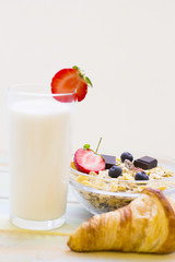 Healthy Breakfast Concept. A glass of milk with a half of strawberry on white, a bowl of cereals with berries and a croissant on white