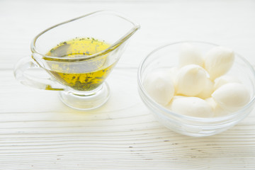 Obraz na płótnie Canvas Preparing Food Concept with a jar of extra virgin olive oil and a bowl of mozarella cheese on a white wooden background, close up