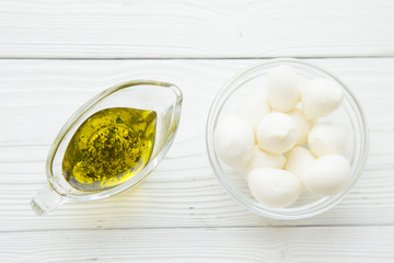 Preparing Food Concept with a jar of extra virgin olive oil and a bowl of mozarella cheese on a white wooden background, close up