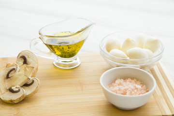 Preparing Food Concept with a jar of extra virgin olive oil, sliced champignone mushroom, natural sea salt and a bowl of mozarella cheese on a white wooden background, close up