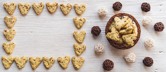 Homemade cookies with turmeric and flax seeds in the form of heart on white boards with a basket and tangles of vine.