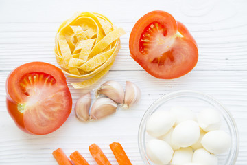 Preparing Food Concept. Ingredients for cooking fettuccini with garlic, mozzarella cheese and fresh vegetables, white wooden background, top view