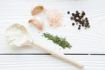 Preparing Food Concept. Ingredients for cooking:wooden spoon of flour, garlic cloves, herbs and spices on white wooden background, top view