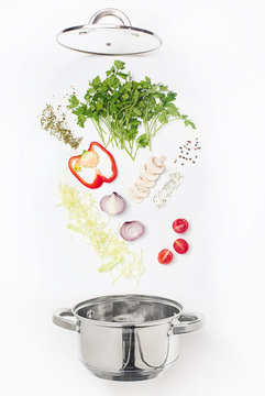 Assorted fresh vegetables falling into a bowl, on white background