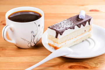 Slice of delicious sweet layered glaze cake and cup of coffee on the wooden table