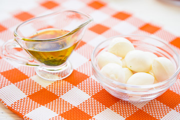 Preparing Healthy Food, Kitchen Concept. Cooking ingredients on an orange plaid cloth: a jar of olive oil and a bowl of mozarellaa cheese, close up