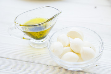 Preparing Healthy Food, Kitchen Concept. Cooking ingredients on awhite wooden table: a jar of olive oil and a bowl of mozarellaa cheese, close up