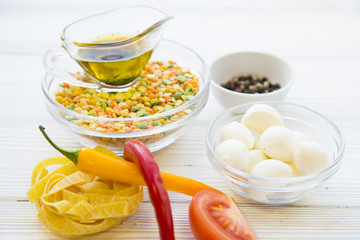Preparing Healthy Food, Kitchen Concept. Cooking ingredients on awhite wooden table: olive oil, bowls with mozarella and beans, fetuccini, chili peppers and spices