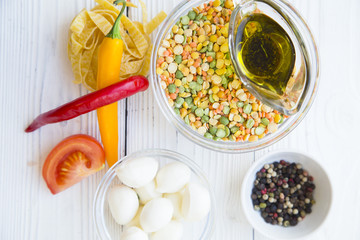 Preparing Healthy Food, Kitchen Concept. Cooking ingredients on awhite wooden table: olive oil, bowls with mozarella and beans, fetuccini, chili peppers and spices, top view