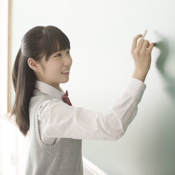 チョークで黒板に文字を書く女子校生
