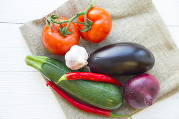 Preparing Healthy Food, Vegeterian, Vegan Concept. A set of fresh whole vegetables: zuccini, eggplant, tomatoes, chilli peppers, red onion and garlic on a white wooden tablle, top view