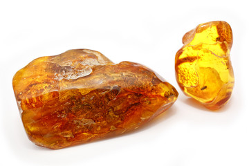 Two pieces of bright amber of different transparency red and yellow on a white background. Crystals of amber as a natural mineral for making jewelry. Sunstone. Macro photo  of amber with Inclusions