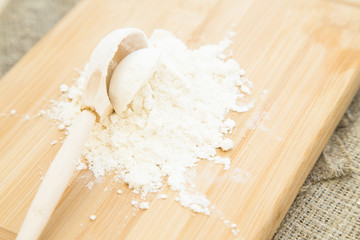 Kitchen, Baking, Pastry Concept. A wooden cutting board with a heap of flour and a wooden spoon on a linen cloth, a garlic bulb and fetuccini nests, close up