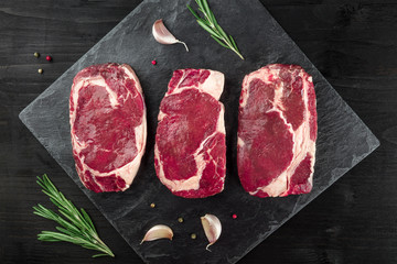 Three slices of raw meat on black with seasoning