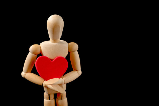 Wooden man figure holding red heart. Wooden human dummy on a black background with copy space for your text. Concept for valentine's day celebration or couple of love.