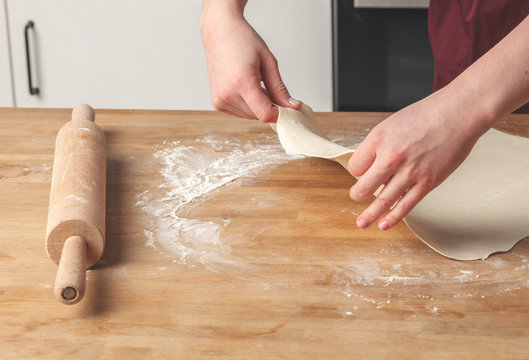 View on housewife making dough cooking pastry with rustic rolling pin spread with flour over wooden table