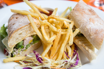 Sandwich with ham, cheese and golden French fries potatoes on a white plate