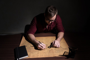A guy with glasses examines a map of the world through a magnifying glass