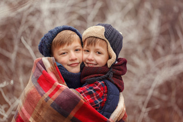 Two smiling brothers hugging each other covered with a warm blanket on a winter day.