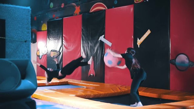 Two pretty young woman in trampolin acrobatic hall plays ball, slow-motion