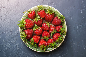 Ripe red strawberry on a plate over black modern background, top view, flatlay