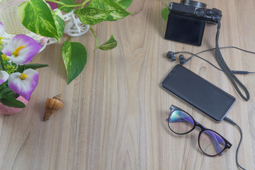 Minimal flat lay Smartphone with earphones and glasses, camera, shell,flower, green leaves on wooden table in garden with copy space, concept relaxing background.