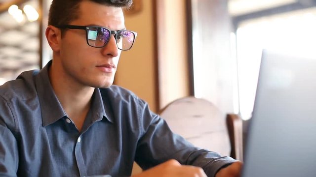 Reflections of laptop monitor screen in man's glasses. Portrait of young caucasian freelancer businessman working and browsing internet in office. Hacker at work stealing accounts database.