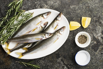 Fresh small sea fish smelt, sardine on a simple background with salt, rosemary and lemon slices. Top view. The concept of healthy sea food,