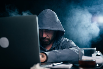 A computer hacker is typing on a laptop in a smoky room. Dark background