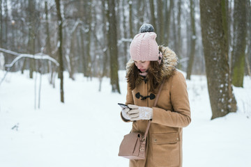 Cute young woman looking for a road map on a smartphone in a winter forest