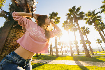 young smiling woman tilting her head against a background of palms and sunset looking into the sunset