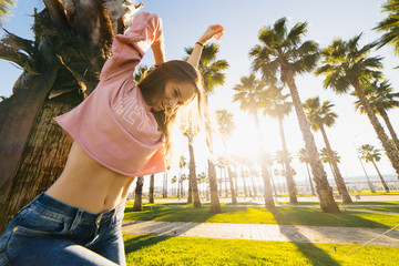 young happy smiling woman against the backdrop of palms and sunset rejoicing