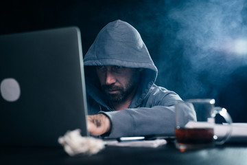 A computer hacker is typing on a laptop in a smoky room. Dark background