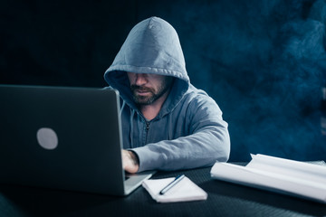 A computer hacker is typing on a laptop in a smoky room. Dark background